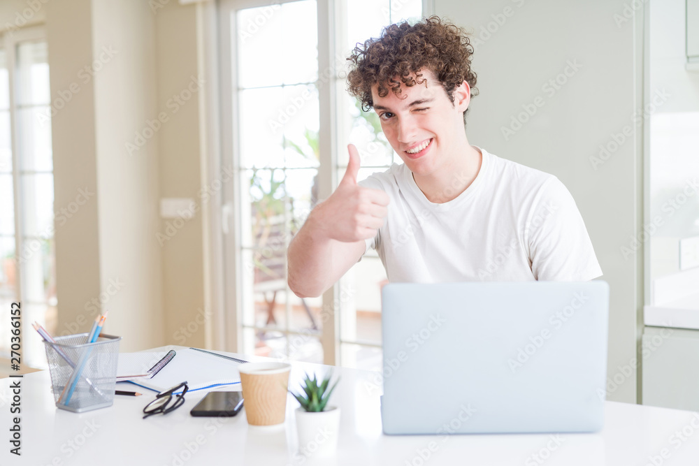Young student man working and studying using computer laptop happy with big smile doing ok sign, thumb up with fingers, excellent sign