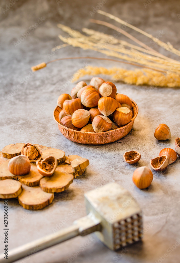 Hazelnuts in the shell in a small bowl and nutcracker. On a gray background.