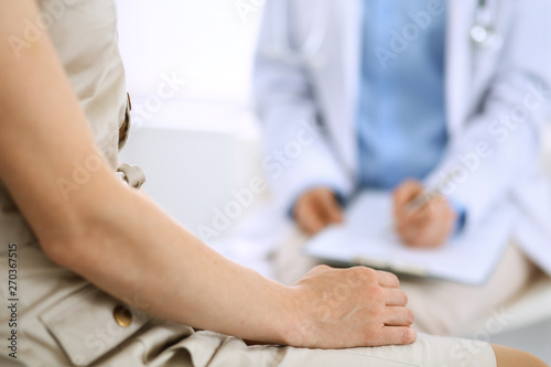 Doctor and patient talking. Physician at work in hospital while writing up medication history records form on clipboard near sitting woman. Healthcare and medicine concepts © rogerphoto
