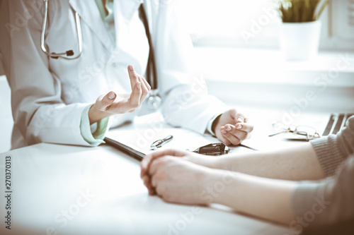 Doctor and female patient sitting at the desk and talking in clinic near window. Medicine and health care concept. Green is main color