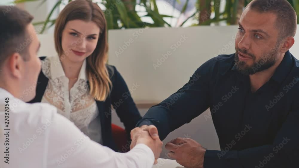Young salesman giving keys of car to buyer. Men shaking hands in car dealership. Young couple happy with the purchase