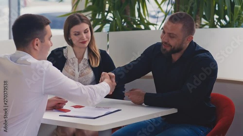 Beautiful couple in car dealership. Young salesman giving keys of car to buyer. Men shaking hands in car dealership