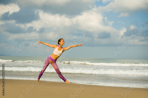 young happy and attractive woman in yoga pants stretching and doing flexibility and meditation exercise at beautiful beach in wellness and healthy natural lifestyle