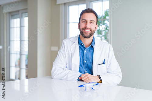 Handsome scientist man wearing white robe and safety glasses with a happy and cool smile on face. Lucky person. © Krakenimages.com