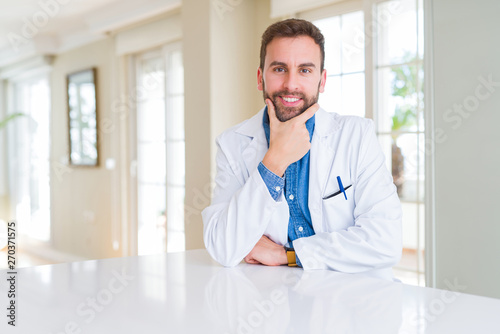 Handsome doctor man wearing medical coat at the clinic looking confident at the camera with smile with crossed arms and hand raised on chin. Thinking positive.