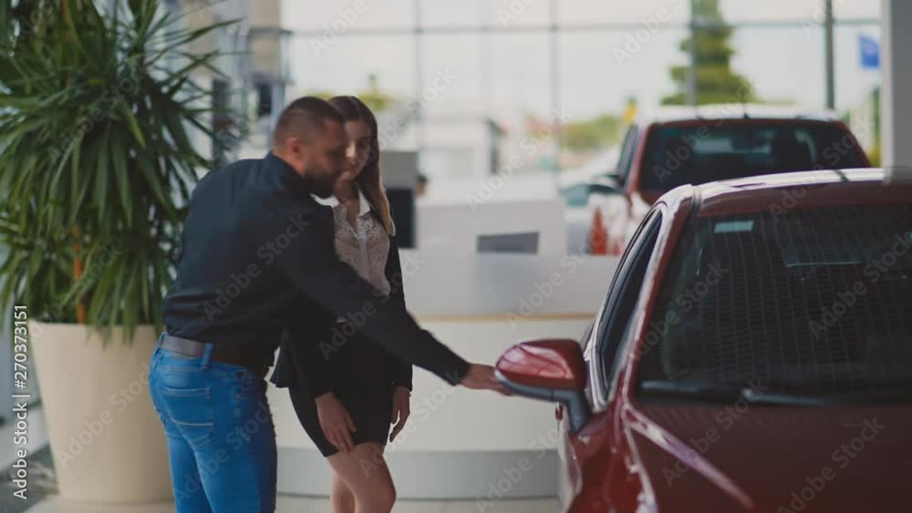 Beautiful couple walking in the car dealership salon looking at the cars choosing a vehicle to buy Beautiful couple walking in the car dealership salon looking at the cars choosing a vehicle to buy