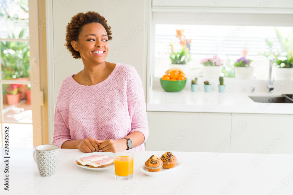 Young african american woman eating breaksfast in the morning at home looking away to side with smile on face, natural expression. Laughing confident. Young african american woman eating breaksfast in the morning at home looking away to side with smile on face, natural expression. Laughing confident.