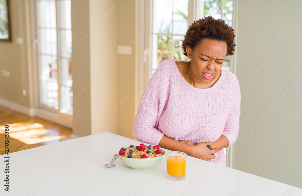 Young african american woman having healthy breakfast in the morning at home with hand on stomach because nausea, painful disease feeling unwell. Ache concept.