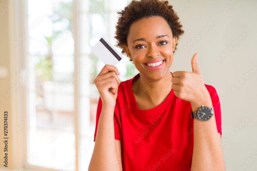 Young african american woman holding credit card happy with big smile doing ok sign, thumb up with fingers, excellent sign