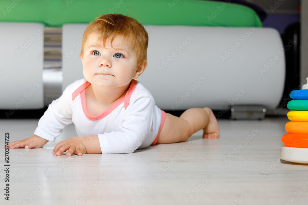 Naklejka premium Little cute baby girl learning to crawl. Healthy child crawling in kids room. Smiling happy healthy toddler girl. Cute toddler discovering home and learning different skills