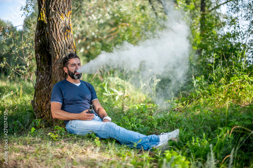 Stylish vape man blows up a couple an electronic cigarette in the forest. Handsome man.