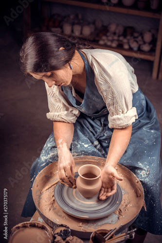 Charming young and cheerful woman works with clay on a potter's wheel. Handicraft. photo