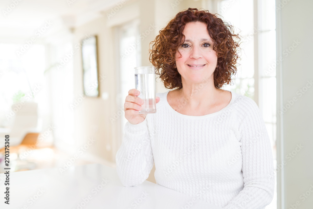 Senior woman driking a fresh glass of water with a happy face standing and smiling with a confident smile showing teeth Senior woman driking a fresh glass of water with a happy face standing and smiling with a confident smile showing teeth
