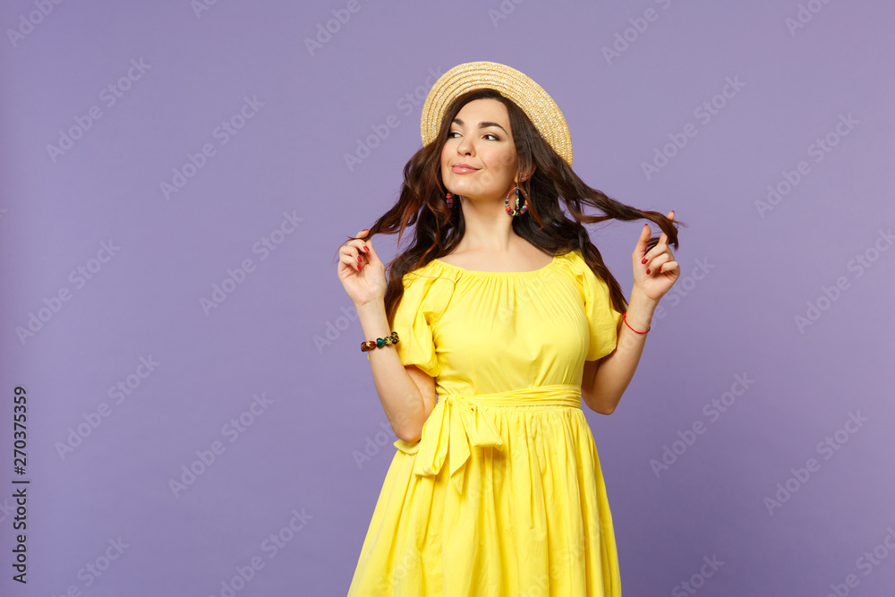 Portrait of pretty smiling young woman in yellow dress, summer hat holding hair looking aside isolated on pastel violet wall background. People sincere emotions, lifestyle concept. Mock up copy space. Portrait of pretty smiling young woman in yellow dress, summer hat holding hair looking aside isolated on pastel violet wall background. People sincere emotions, lifestyle concept. Mock up copy space.