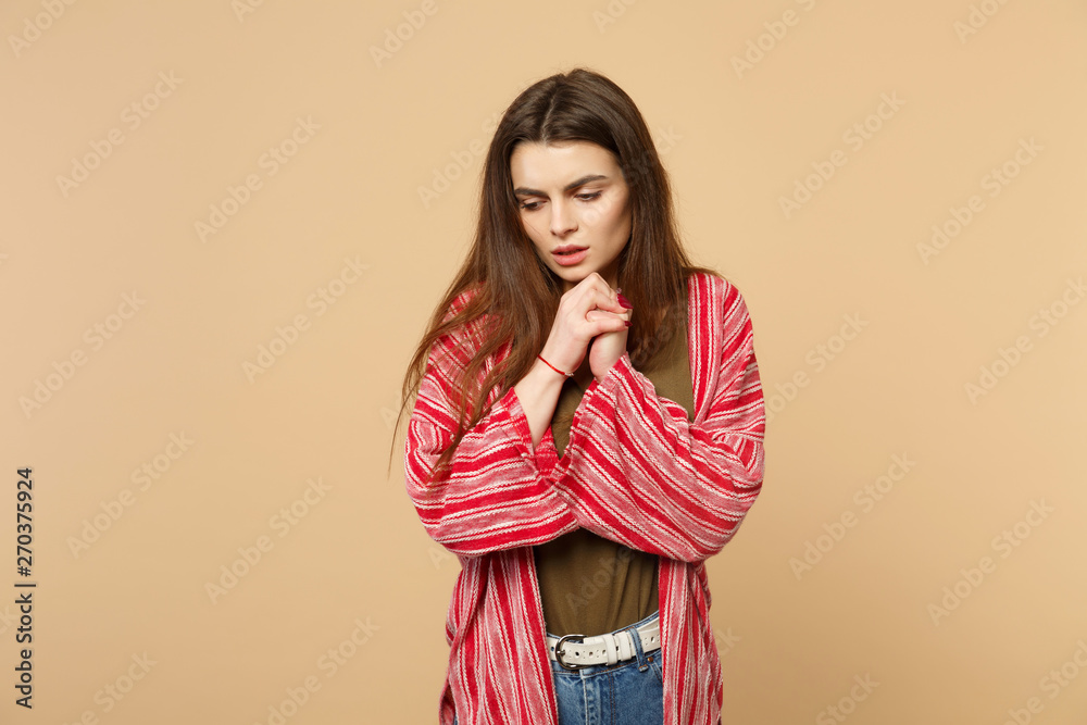 Portrait of worried upset young woman in casual clothes looking down, holding hands isolated on pastel beige wall background in studio. People sincere emotions, lifestyle concept. Mock up copy space. Portrait of worried upset young woman in casual clothes looking down, holding hands isolated on pastel beige wall background in studio. People sincere emotions, lifestyle concept. Mock up copy space.