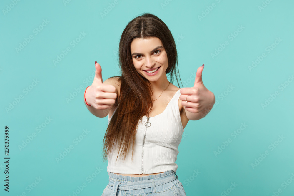 Portrait of smiling beautiful young woman in light casual clothes showing thumbs up isolated on blue turquoise wall background in studio. People sincere emotions lifestyle concept. Mock up copy space. Portrait of smiling beautiful young woman in light casual clothes showing thumbs up isolated on blue turquoise wall background in studio. People sincere emotions lifestyle concept. Mock up copy space.