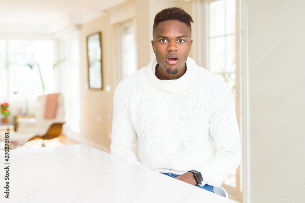 Handsome african american man on white table afraid and shocked with surprise expression, fear and excited face. Handsome african american man on white table afraid and shocked with surprise expression, fear and excited face.