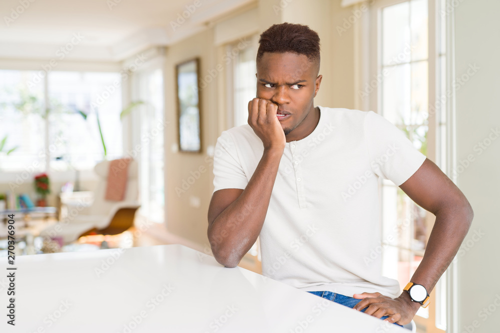 Handsome african american man on white table at home looking stressed and nervous with hands on mouth biting nails. Anxiety problem.