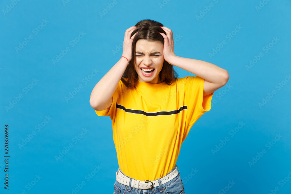 Portrait of frustrated screaming young woman in vivid casual clothes keeping eyes closed putting hands on head isolated on blue wall background in studio. People lifestyle concept. Mock up copy space. Portrait of frustrated screaming young woman in vivid casual clothes keeping eyes closed putting hands on head isolated on blue wall background in studio. People lifestyle concept. Mock up copy space.