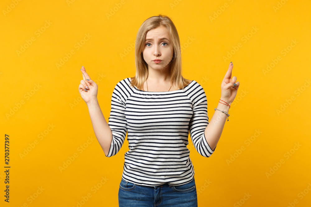 Concerned young woman in striped clothes waiting for special moment, keeping fingers crossed making wish isolated on yellow orange background. People emotions, lifestyle concept. Mock up copy space. Concerned young woman in striped clothes waiting for special moment, keeping fingers crossed making wish isolated on yellow orange background. People emotions, lifestyle concept. Mock up copy space.