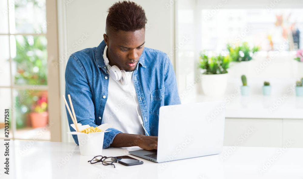 Handsome young african business man eating delivery asian food and working using computer concentrated Handsome young african business man eating delivery asian food and working using computer concentrated