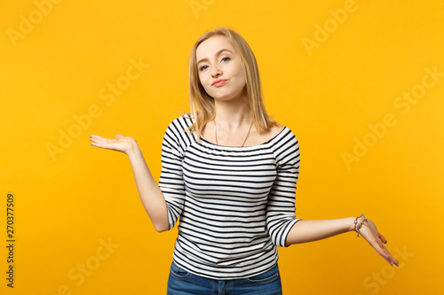 Arrogant haughty young woman in striped clothes spreading, pointing hands aside isolated on yellow orange wall background in studio. People sincere emotions, lifestyle concept. Mock up copy space.