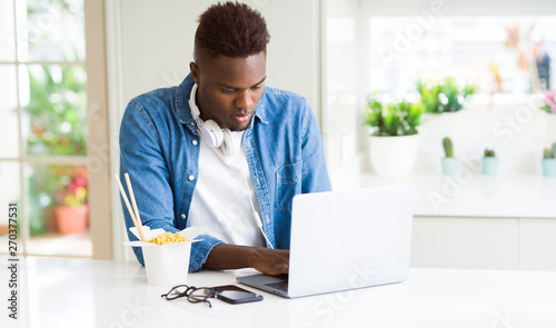 Handsome young african business man eating delivery asian food and working using computer concentrated