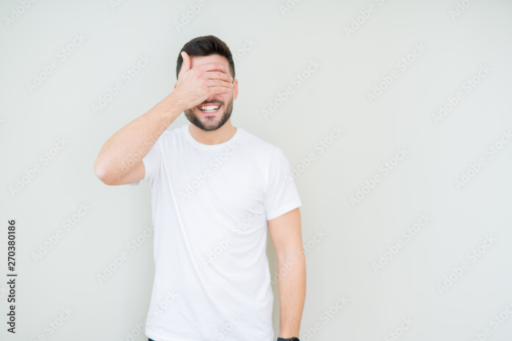 Young handsome man wearing casual white t-shirt over isolated background smiling and laughing with hand on face covering eyes for surprise. Blind concept. Young handsome man wearing casual white t-shirt over isolated background smiling and laughing with hand on face covering eyes for surprise. Blind concept.