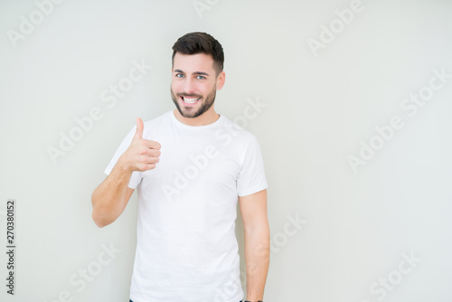 Young handsome man wearing casual white t-shirt over isolated background doing happy thumbs up gesture with hand. Approving expression looking at the camera showing success.