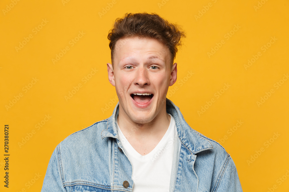 Portrait of cheerful excited young man wearing denim casual clothes looking camera isolated on yellow orange wall background in studio. People sincere emotions, lifestyle concept. Mock up copy space. Portrait of cheerful excited young man wearing denim casual clothes looking camera isolated on yellow orange wall background in studio. People sincere emotions, lifestyle concept. Mock up copy space.