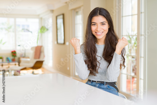 Free Download Young beautiful woman at home celebrating surprised and amazed for success with arms raised and open eyes. Winner concept. - GFXLoad