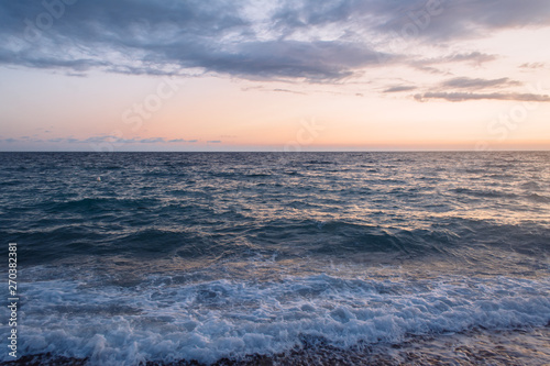 Sea waves at sunset. Wallpaper with ocean sunset. Sky filled with beautiful pastel colors of the sun setting down over the horizon. 