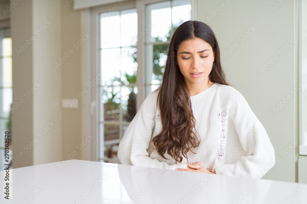 Young beautiful woman at home on white table with hand on stomach because indigestion, painful illness feeling unwell. Ache concept. Young beautiful woman at home on white table with hand on stomach because indigestion, painful illness feeling unwell. Ache concept.