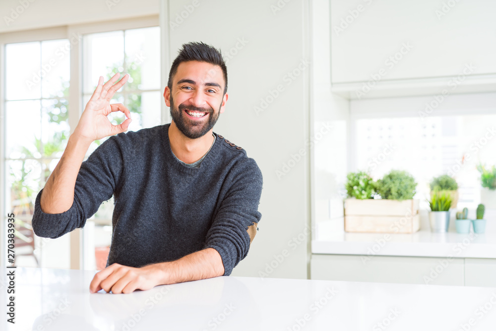 Handsome hispanic man wearing casual sweater at home smiling positive doing ok sign with hand and fingers. Successful expression. Handsome hispanic man wearing casual sweater at home smiling positive doing ok sign with hand and fingers. Successful expression.
