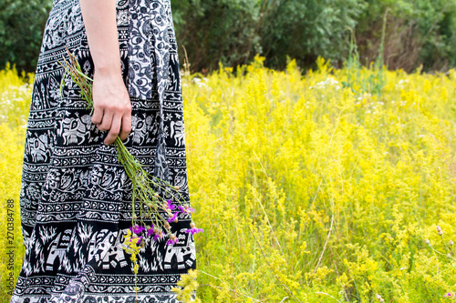 A girl in a long skirt with contrasting patterns holds in her hand wild flowers photo