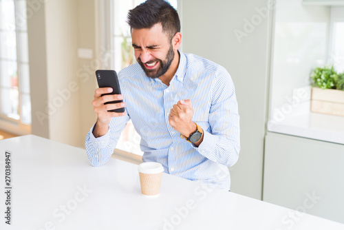 Handsome hispanic business man drinking coffee and using smartphone annoyed and frustrated shouting with anger, crazy and yelling with raised hand, anger concept