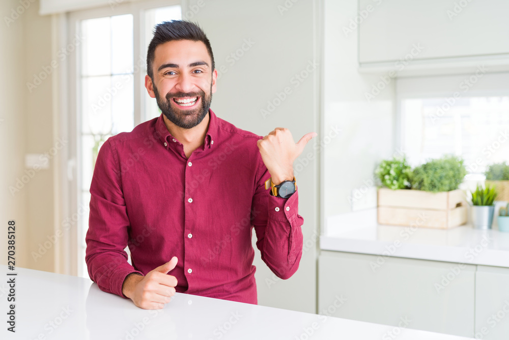 Handsome hispanic business man smiling with happy face looking and pointing to the side with thumb up.