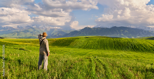 Panorama of a mountain valley in summer. Adult man looks into the distance. Amazing nature, mountains, lit by the sun in clear weather, summer in the mountains. Travel and camping, tourism