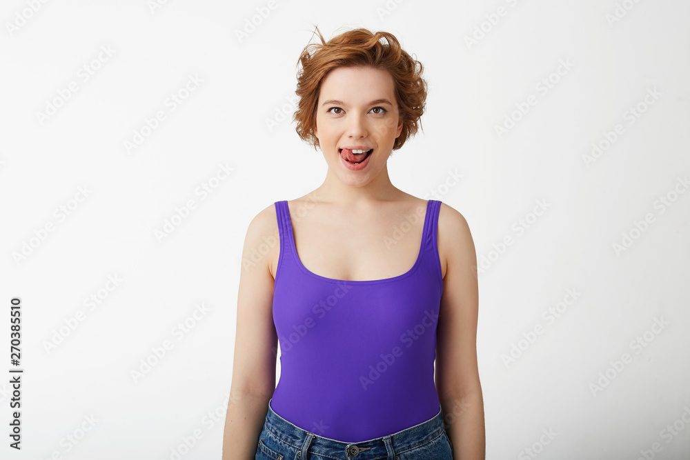 Photo of happy funny young cute short-haired girl, looking at the camera and licking, presenting a delicious dessert, stands over white background. Photo of happy funny young cute short-haired girl, looking at the camera and licking, presenting a delicious dessert, stands over white background.