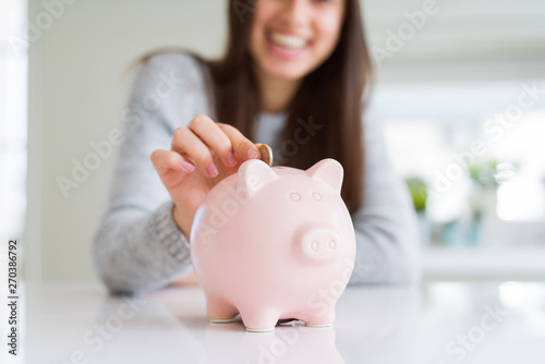 Young woman smiling putting a coin inside piggy bank as savings for investment photo