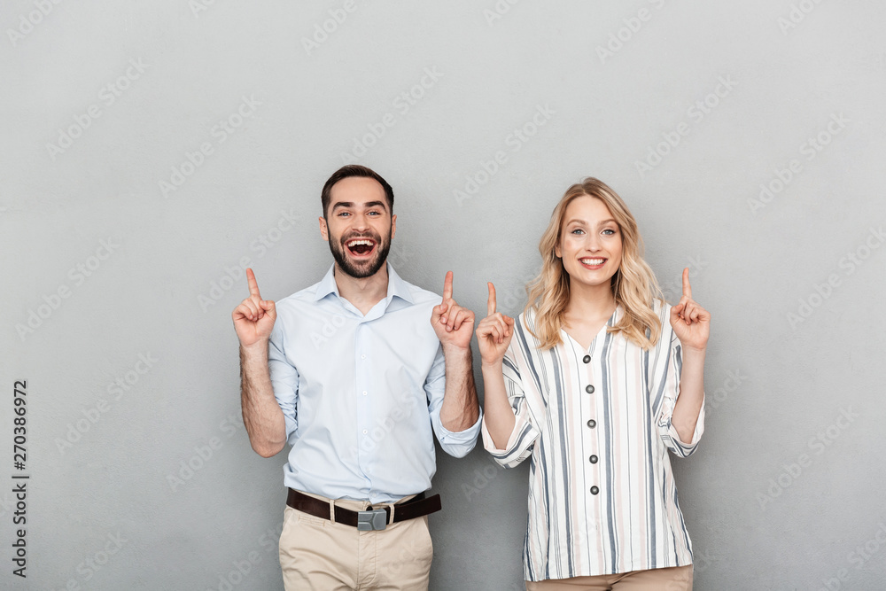 Photo of nice couple in casual clothing smiling while pointing fingers at copyspace - obrazy, fototapety, plakaty 