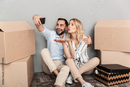 Photo of attractive couple seating near cardboard boxes and taking selfie photo on cellphone © Drobot Dean