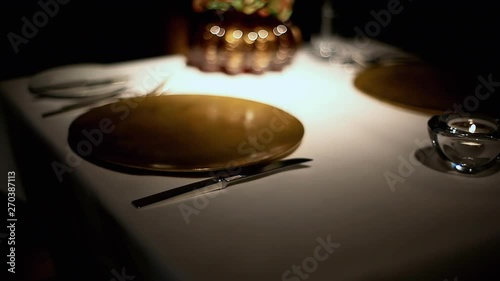 A butler wearing gloves, preparing the table for dinner by carefully adjusting (perfectly aligning) the cutlery and the glass. Dim lights. photo