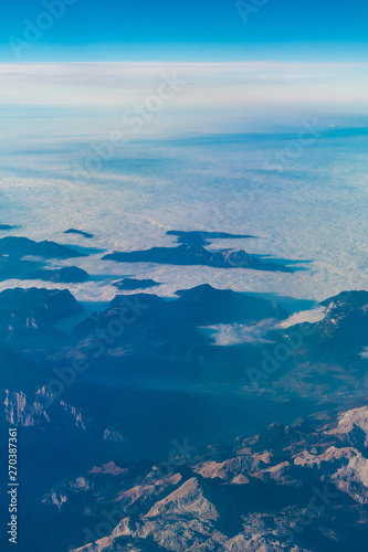View from the porthole of airplane of a beautiful landscape with mountains hiding in the clouds © dr_verner