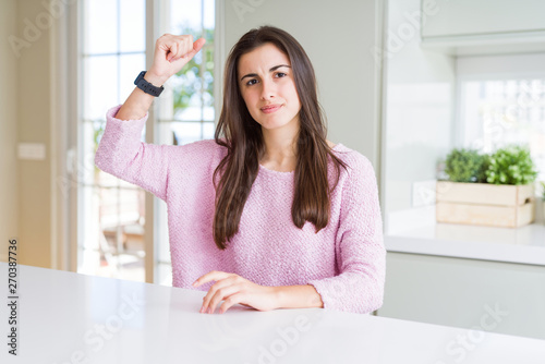 Beautiful young woman wearing pink sweater angry and mad raising fist frustrated and furious while shouting with anger. Rage and aggressive concept.