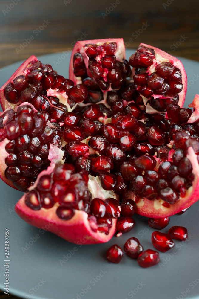 Organic pomegranate on a grey ceramic plate. Dark wooden table, high resolution