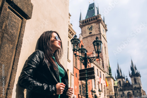 Street portrait of adorable brunette woman in sunglasses posing at Old Town Square in Prague. smiling pretty brunette girl, lifestyle. Old Town Hall with astronomical clock tower in Prague, Czech © Stanislav