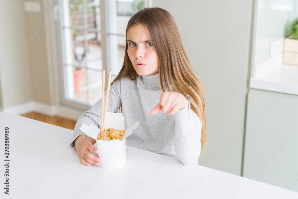 Beautiful young girl kid eating asian rice in delivery box pointing with finger to the camera and to you, hand sign, positive and confident gesture from the front