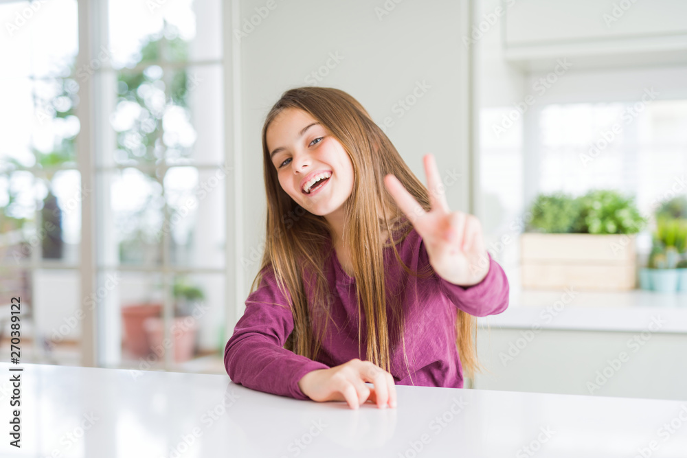 Beautiful young girl kid on white table smiling looking to the camera showing fingers doing victory sign. Number two. Beautiful young girl kid on white table smiling looking to the camera showing fingers doing victory sign. Number two.