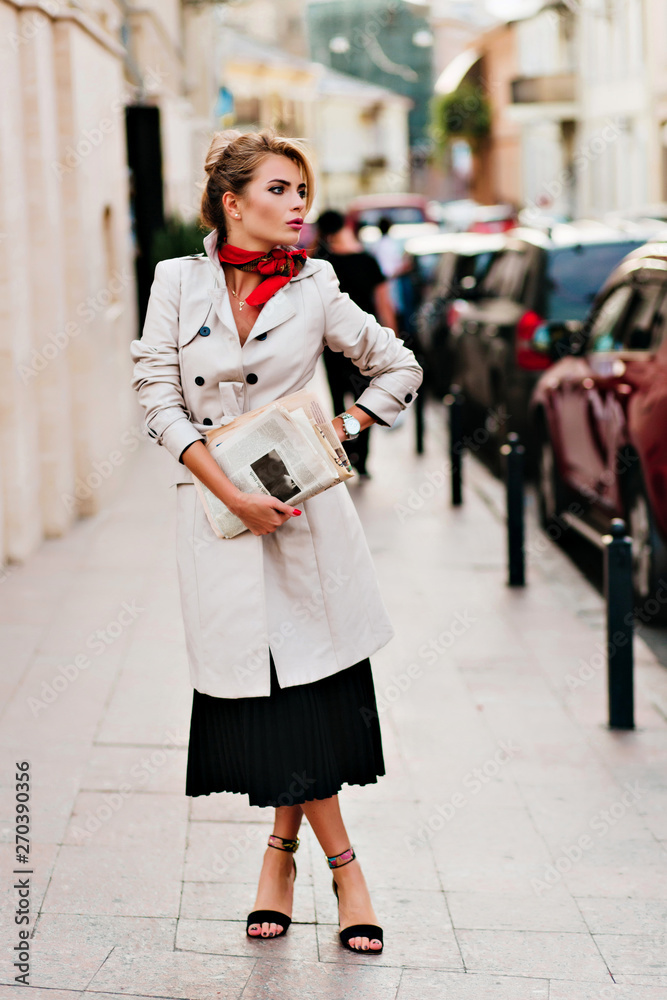 Charming lady with elegant hairstyle waiting someone on the street and looking around. Full-length portrait of worried young woman in coat holding newspaper and posing near cars. Charming lady with elegant hairstyle waiting someone on the street and looking around. Full-length portrait of worried young woman in coat holding newspaper and posing near cars.